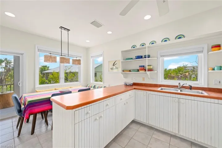 Kitchen with decorative light fixtures, a peninsula, open shelves, stainless steel dishwasher, and light tile patterned floors