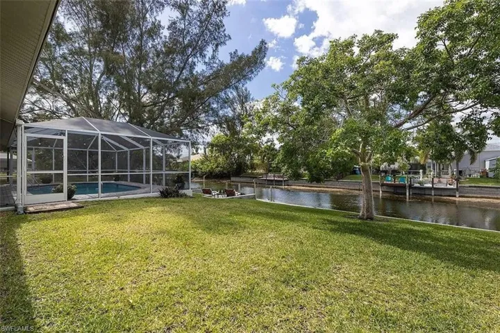 Expansive lawn area featuring a screened pool enclosure with a pool, a water canal, and multiple boat docks