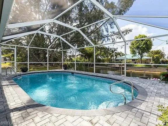 Screened pool enclosure featuring a curved swimming pool, paver deck, and canal access