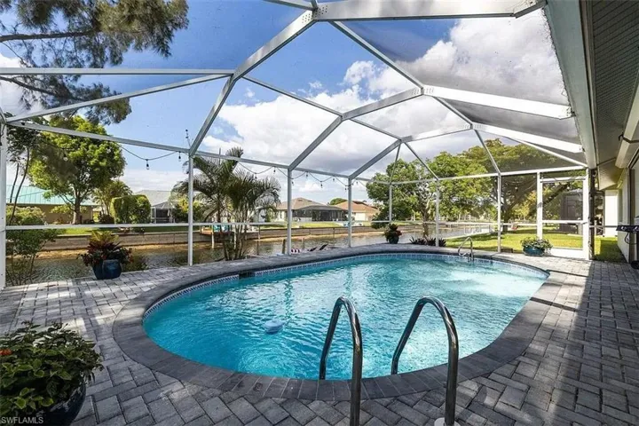 Screened enclosure featuring an oval swimming pool with integrated steps, surrounded by paver patio surfacing, and bordered by a canal