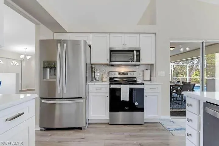 Kitchen features stainless steel appliances, white cabinetry, wood-finish flooring, and a white backsplash