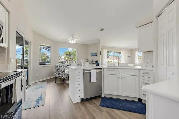White kitchen cabinetry with stainless steel appliances, stone countertops, and wood-finish flooring
