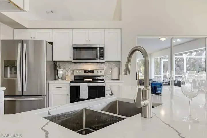 Kitchen featuring white cabinetry, stainless steel appliances, a double basin sink, and a high-arch faucet