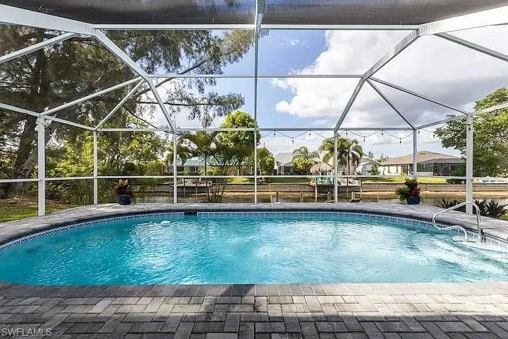Screened pool enclosure featuring a curved swimming pool, paver pool deck, and integrated pool steps with handrail