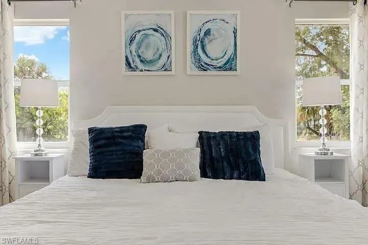 White arched headboard, symmetrical window placement, and two-tier nightstands