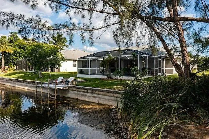Waterfront property featuring a private dock, concrete seawall, expansive screened lanai, and lush green lawn