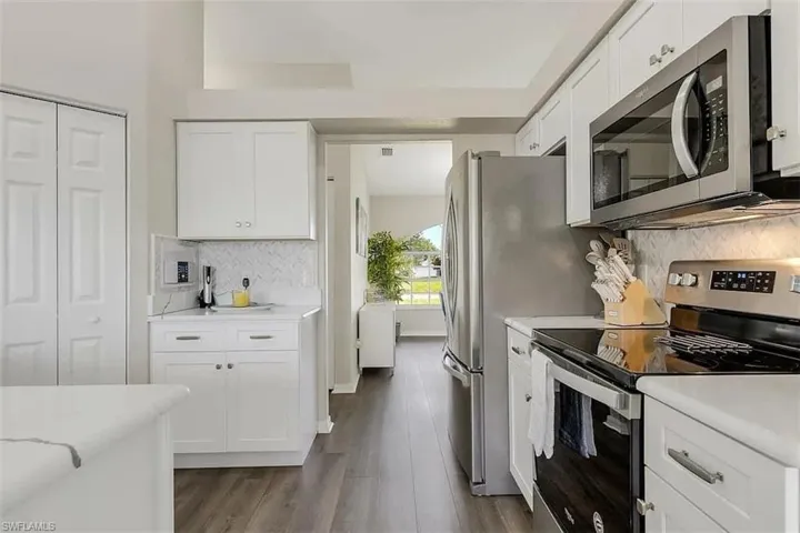 White cabinetry, stainless steel appliances, wood-finish flooring, white countertops, and a white tile backsplash