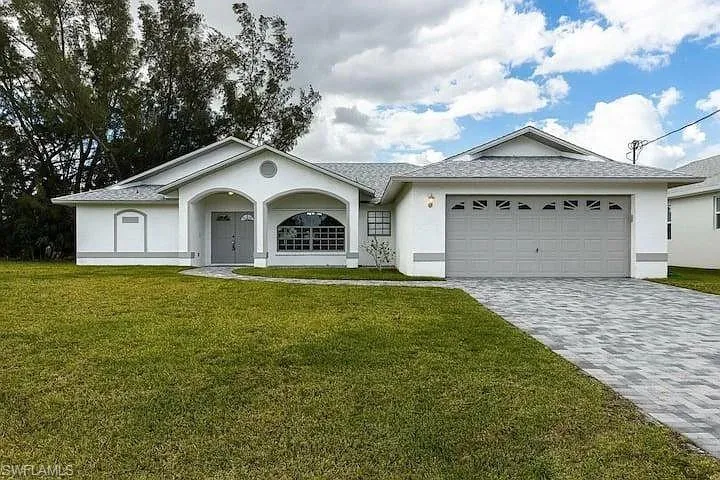 White stucco exterior with a gray trim, arched entryway, decorative window, and an attached two-car garage