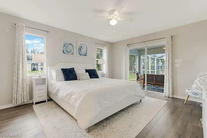 Wood-finish flooring with a ceiling fan, dual windows, and sliding glass doors opening to a screened patio