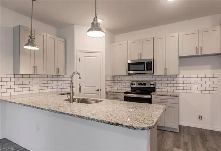 Kitchen featuring granite countertops, subway tile backsplash, stainless steel appliances, pendant lighting, and wood-finish flooring
