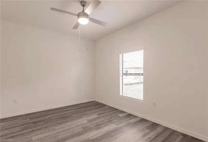 Spacious room featuring gray wood-finish flooring, white walls, and a window with blinds