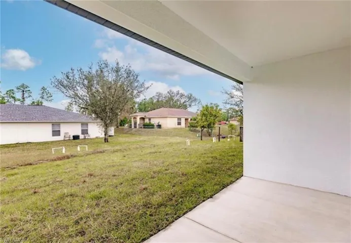 Expansive backyard with a level lawn and mature trees, featuring a concrete patio slab extending from the structure