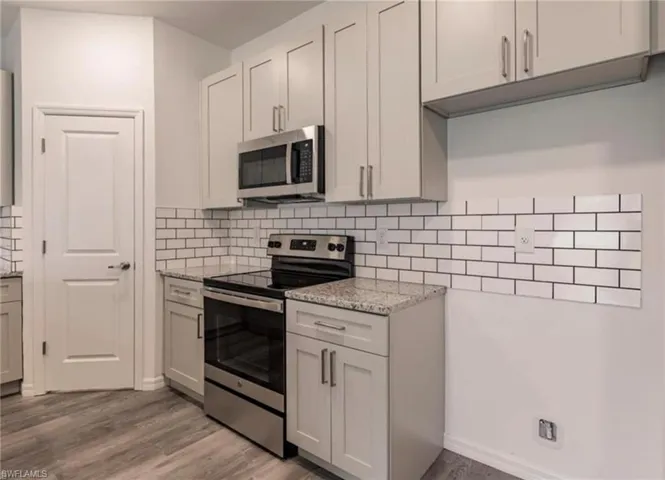 Modern kitchen featuring light gray cabinetry, stainless steel appliances, granite countertops, and a white subway tile backsplash