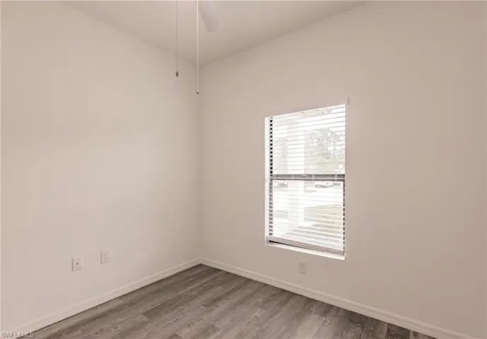 Room featuring wood-finish flooring, white baseboards, a single window with horizontal blinds, and a ceiling fan