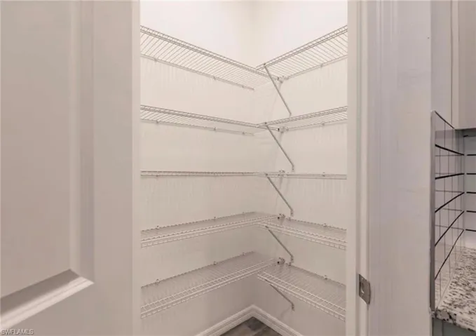 Corner pantry featuring multiple levels of wire shelving, white wall finishes, and wood-finish flooring
