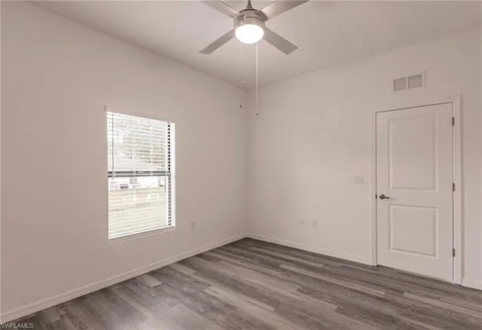 Bright room featuring wood-finish flooring, a contemporary ceiling fan with integrated lighting, and a white paneled door