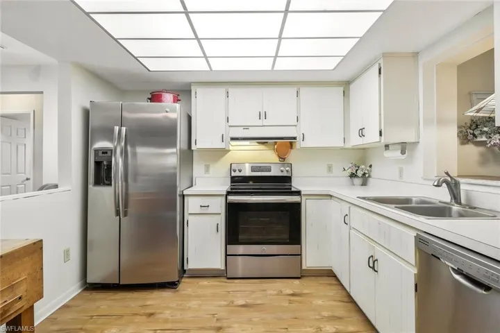 Kitchen featuring range hood, a sink, light wood-type flooring, light countertops, and appliances with stainless steel finishes