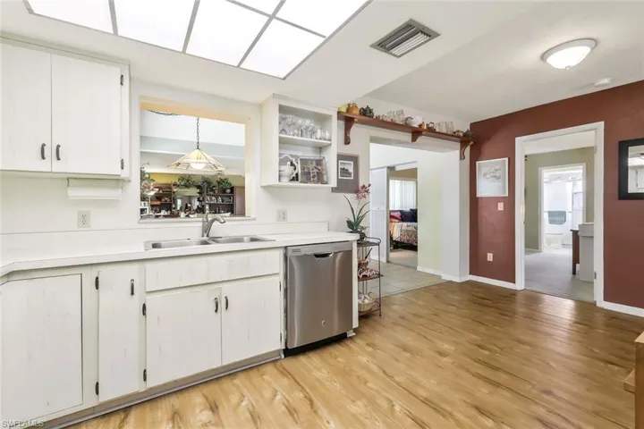 Kitchen featuring a sink, dishwasher, light countertops, white cabinetry.