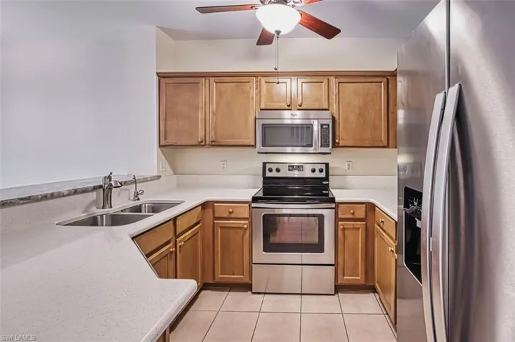 Kitchen with stainless steel appliances, light tile patterned floors, a ceiling fan, and brown cabinetry