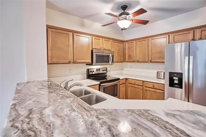 Kitchen with stainless steel appliances, a ceiling fan, quartz countertops and extended marble counter for eating