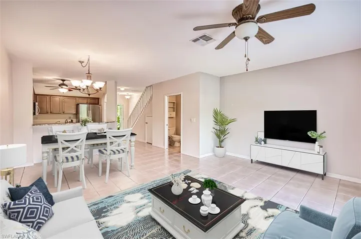 Living area featuring a ceiling fan, light tile patterned floors, stairway, and a chandelier. Virtually Staged