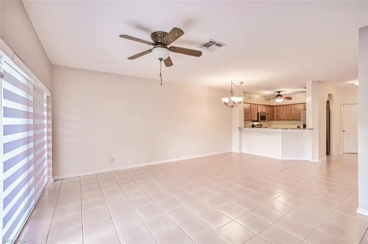 Unfurnished living room featuring a ceiling fan, arched walkways, light tile patterned flooring, and a chandelier