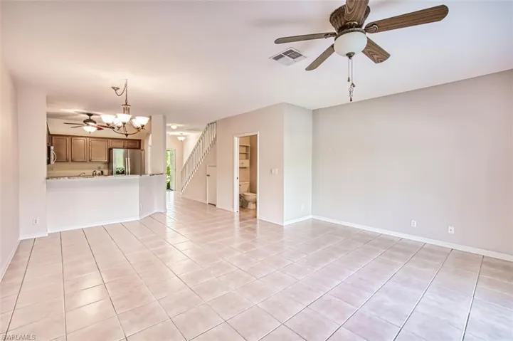 Unfurnished living room with light tile patterned floors, a ceiling fan, a chandelier, and stairs
