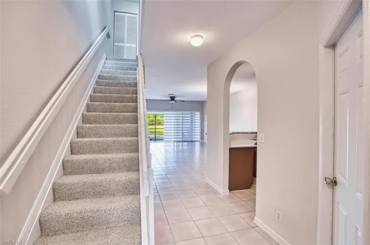 Stairway with arched walkways, tile patterned floors, and ceiling fan