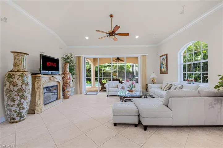 Living area with ceiling fan, recessed lighting, crown molding, light tile patterned flooring, and a glass covered fireplace