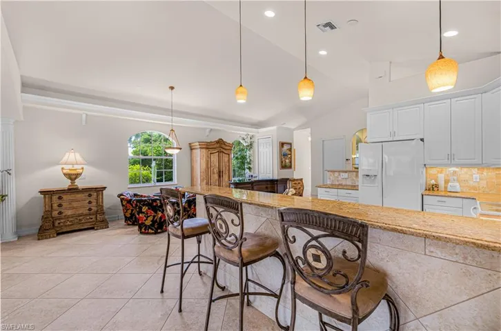 Kitchen with vaulted ceiling, white refrigerator with ice dispenser, a breakfast bar, white cabinetry, and recessed lighting