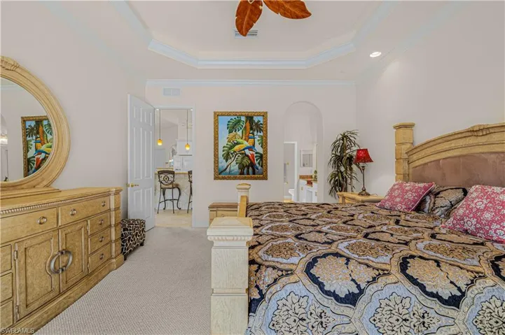 Bedroom with a tray ceiling, ornamental molding, light colored carpet, arched walkways, and ceiling fan