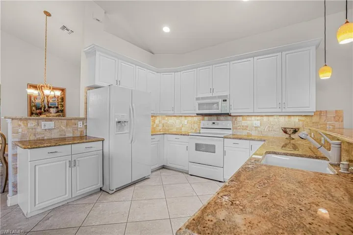 Kitchen with white appliances, a peninsula, vaulted ceiling, a chandelier, and white cabinetry