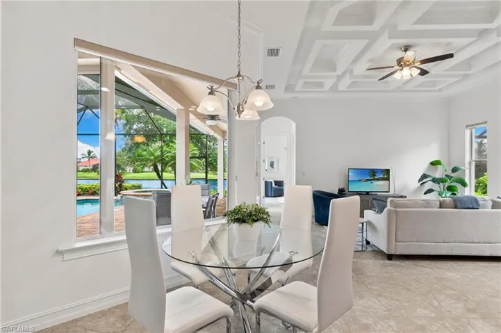 Dining space with arched walkways, a ceiling fan, beam ceiling, coffered ceiling, and a chandelier