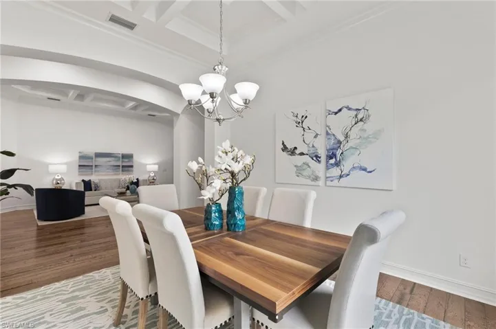 Dining area with coffered ceiling, a chandelier, arched walkways, wood finished floors, and beamed ceiling