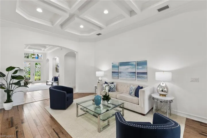 Living area with arched walkways, coffered ceiling, beamed ceiling, ornamental molding, and wood-type flooring