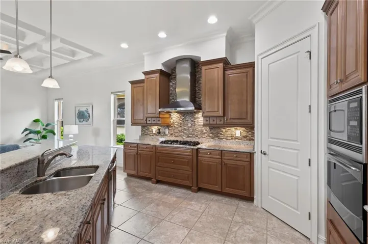 Kitchen with wall chimney exhaust hood, stainless steel appliances, decorative backsplash, light stone countertops, and crown molding
