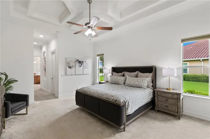 Bedroom featuring coffered ceiling, light carpet, crown molding, beam ceiling, and ensuite bath