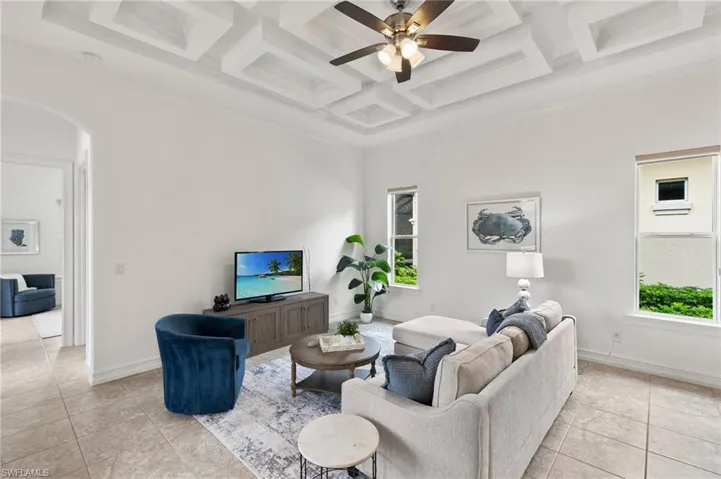 Living room with arched walkways, coffered ceiling, ceiling fan, light tile patterned floors, and beam ceiling