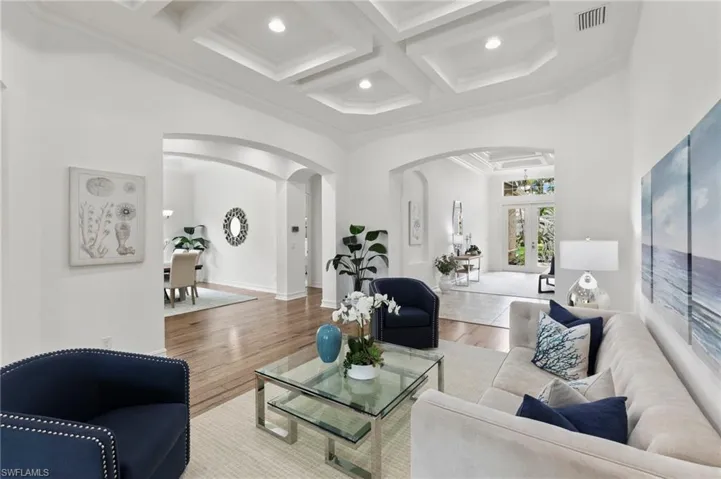 Living room featuring arched walkways, coffered ceiling, wood finished floors, crown molding, and beamed ceiling