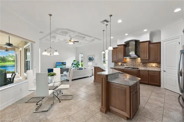 Kitchen with wall chimney exhaust hood, ceiling fan, crown molding, tasteful backsplash, and open floor plan