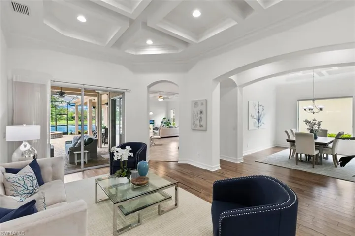 Living area with arched walkways, ceiling fan, wood-type flooring, coffered ceiling, and beam ceiling