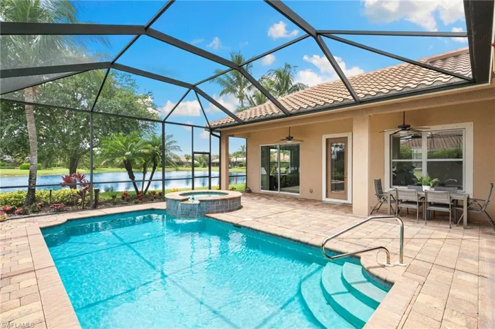 View of pool featuring a ceiling fan, a patio area, a water view, a pool with connected hot tub, and glass enclosure
