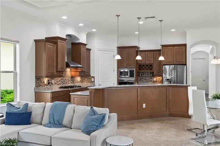 Kitchen featuring stainless steel appliances, wall chimney exhaust hood, arched walkways, open floor plan, and tasteful backsplash