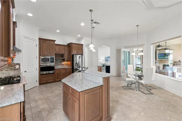 Kitchen with stainless steel appliances, backsplash, a chandelier, arched walkways, and an island with sink
