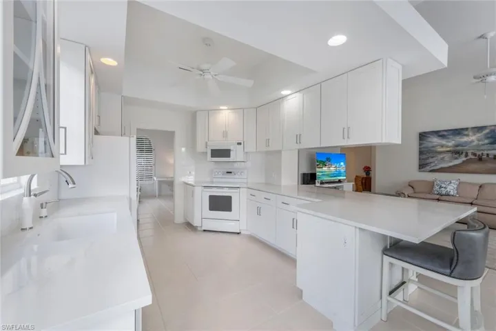 Kitchen featuring a kitchen breakfast bar, ceiling fan, kitchen peninsula, white appliances, and sink