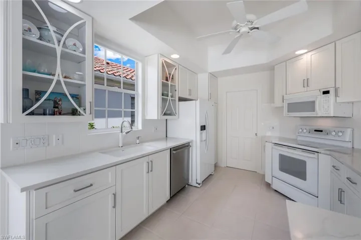 Kitchen with ceiling fan, white appliances, light tile flooring, sink, and white cabinets