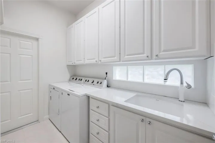 Laundry room with separate washer and dryer, sink, light tile floors, and cabinets