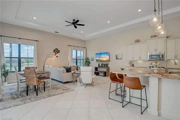 Kitchen featuring light stone countertops, backsplash, open floor plan, a ceiling fan, and stainless steel microwave