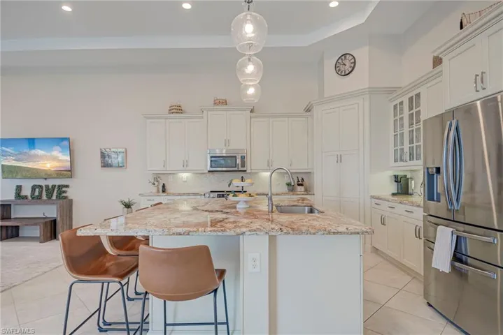 Kitchen featuring stainless steel appliances, light stone countertops, white cabinetry, decorative light fixtures, and a high tray ceiling
