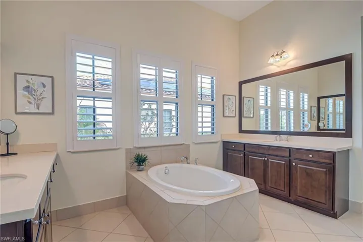 Primary bathroom with two vanities, light tile patterned flooring, a bath, and plenty of natural light